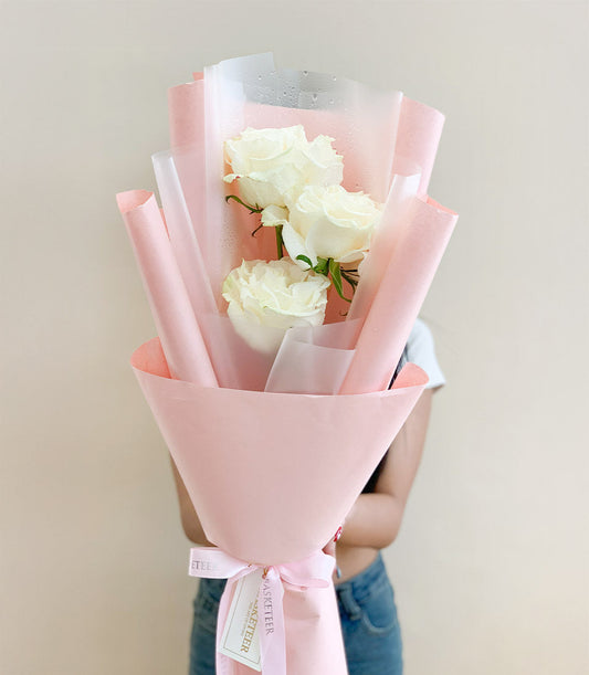 Three fresh white Mondial roses with dewy petals, wrapped in soft pink paper and tied with ribbon