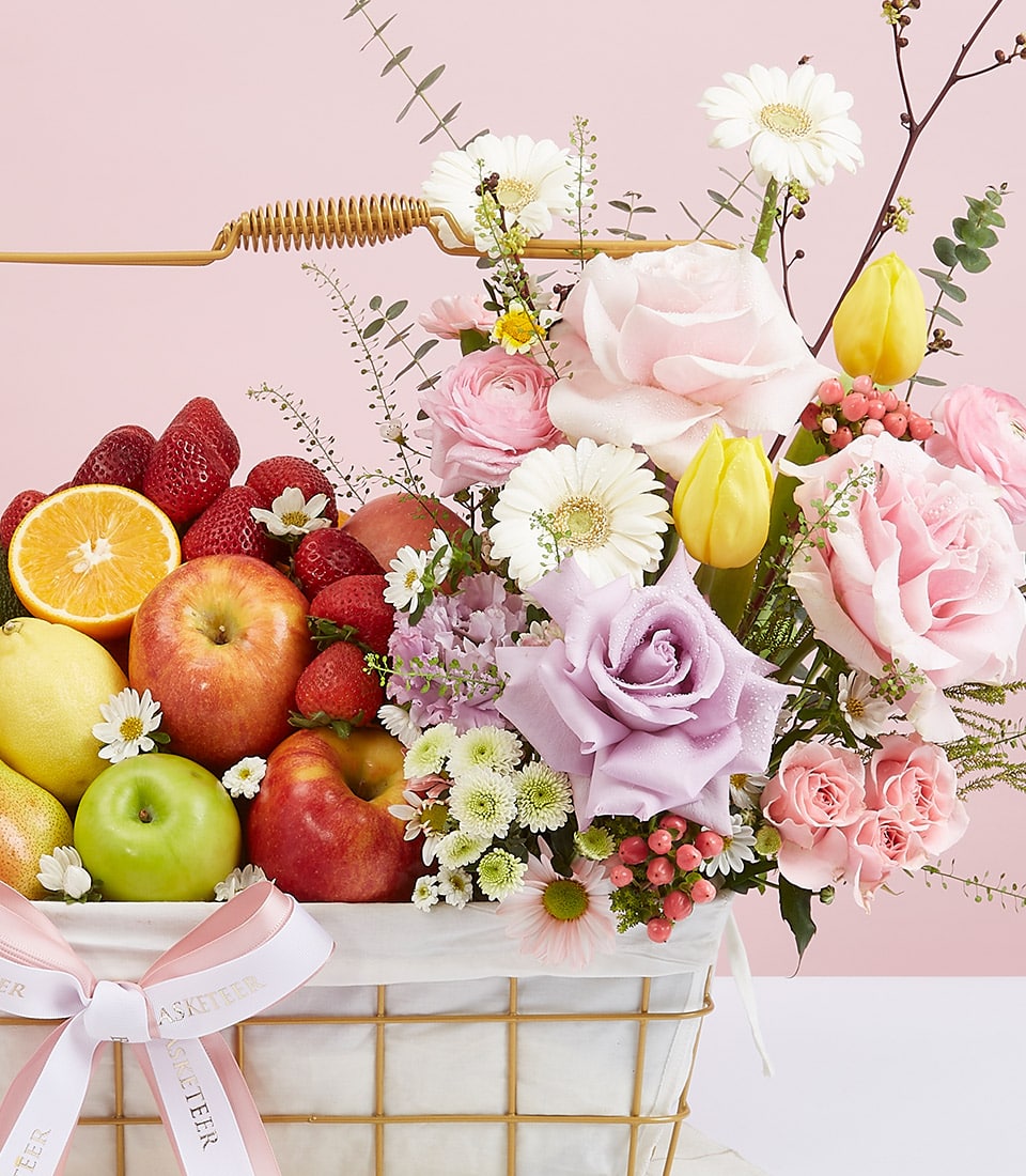 Premium fresh fruit and flower gift basket with roses, gerbera daisies, and seasonal fruits in gold wire frame