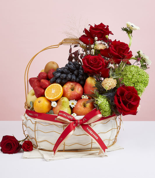 White wire basket with red ribbon, fresh seasonal fruits and vibrant red roses with white anemones for gifting