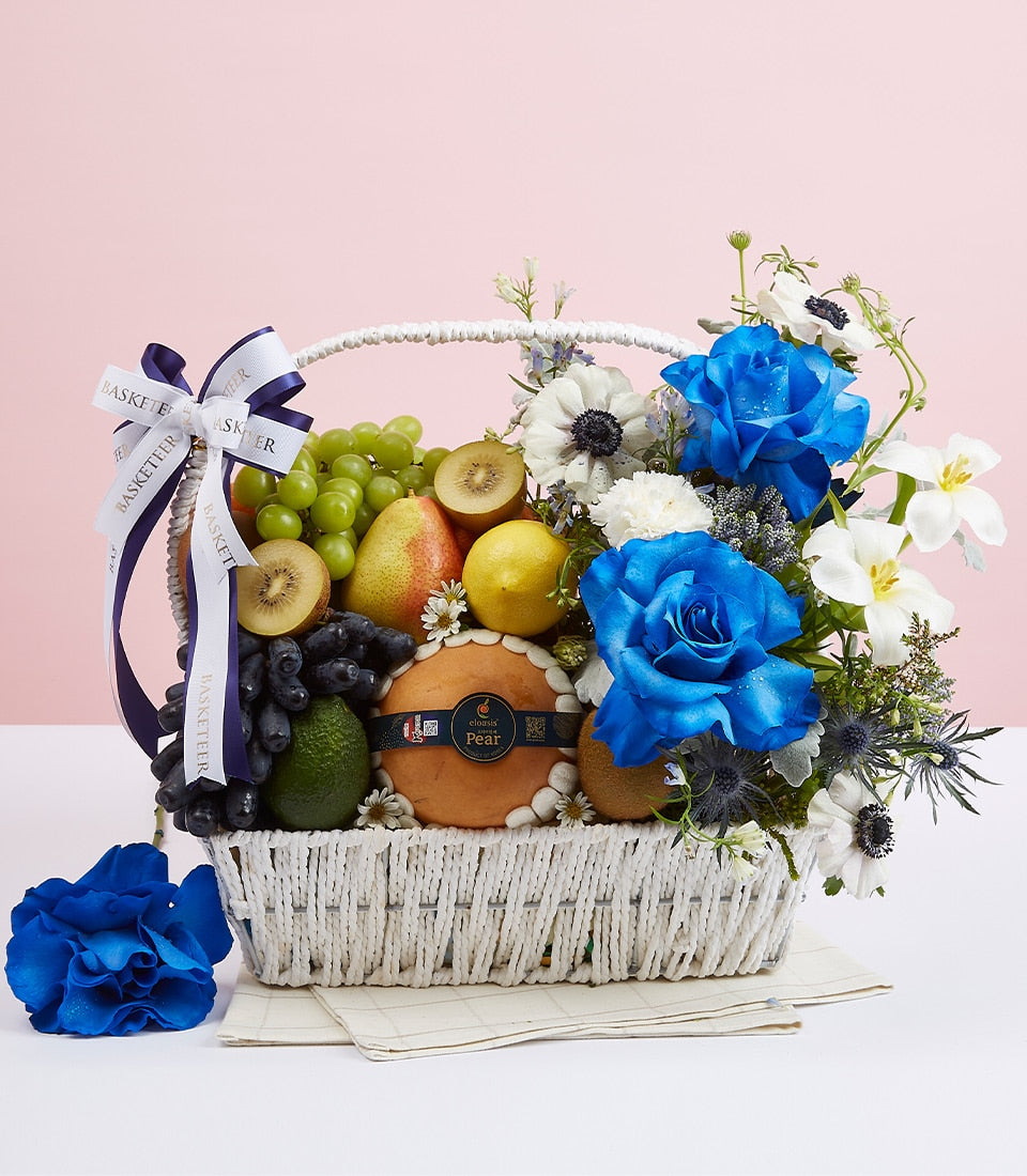 Blue roses and fresh fruit in white woven basket with grapes, kiwi, pear, and lemon arrangement