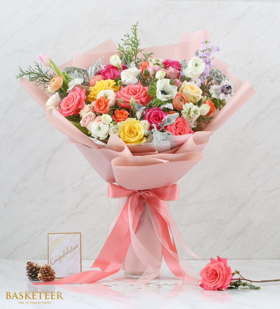 Vibrant mixed roses and flowers in pink, yellow, orange, and white with pink ribbon wrapping and congratulations card