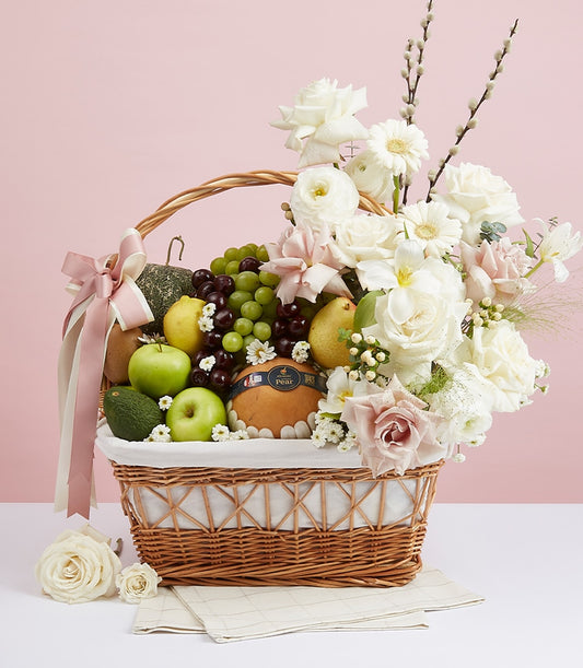 Woven wicker fruit hamper with fresh grapes, apples, pears, and white-pink roses, ranunculus, and greenery