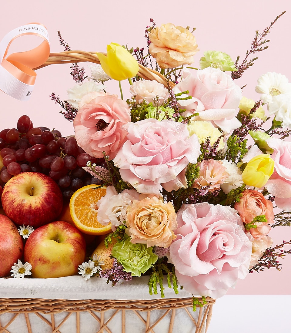Premium wicker basket with fresh roses, ranunculus, tulips, and seasonal fruit for gifting