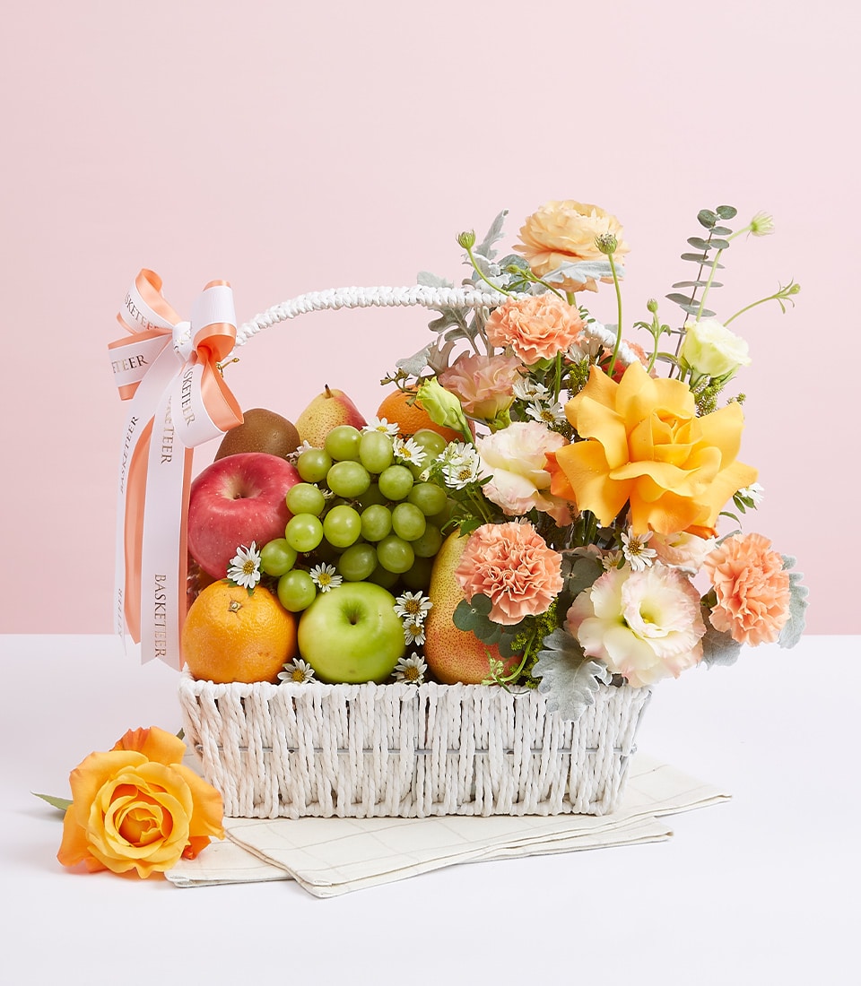 Sunny yellow roses and fresh fruits in white woven basket with peach ribbon, premium gift arrangement