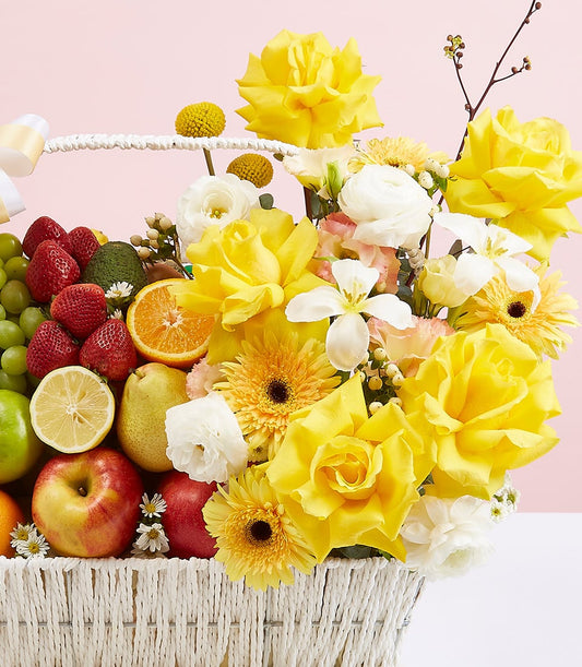 Premium white woven basket with fresh fruit medley and yellow roses, gerbera daisies, and white ranunculus