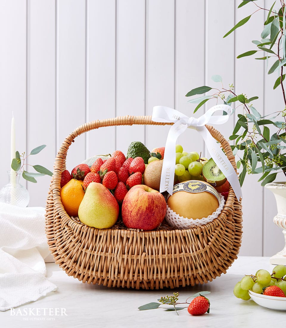 Wicker fruit basket with fresh strawberries, grapes, pears, apples, and kiwi tied with white satin ribbon