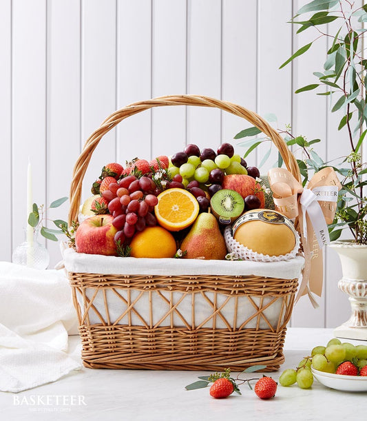 Premium rattan fruit basket with red grapes, strawberries, apples, oranges and pears, beige ribbon handle