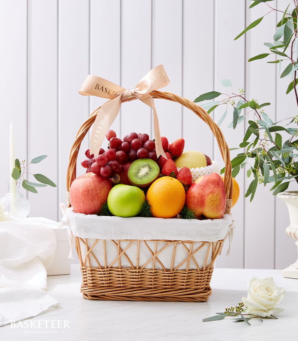 Woven wicker fruit basket filled with fresh grapes, apples, oranges, strawberries, kiwi, and pear