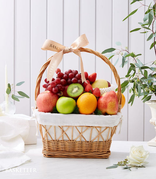 Woven wicker fruit basket filled with fresh grapes, apples, oranges, strawberries, kiwi, and pear