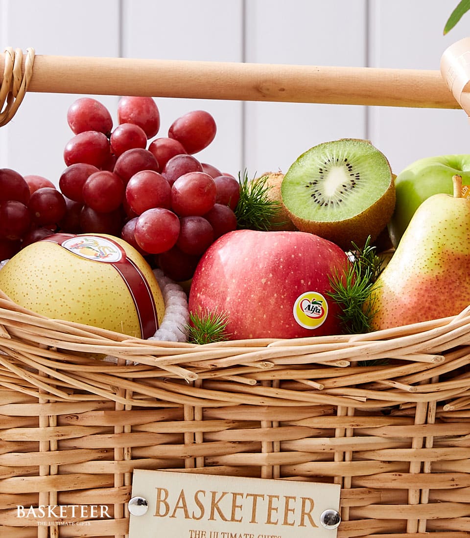 Woven wicker basket filled with fresh red grapes, pears, apples, kiwi, and green foliage