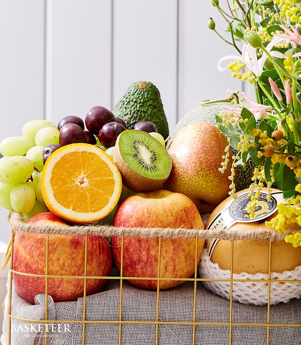 Vibrant fresh fruit and flower basket with yellow mimosa, pink lilies, tropical fruits in gold wire basket with rope trim