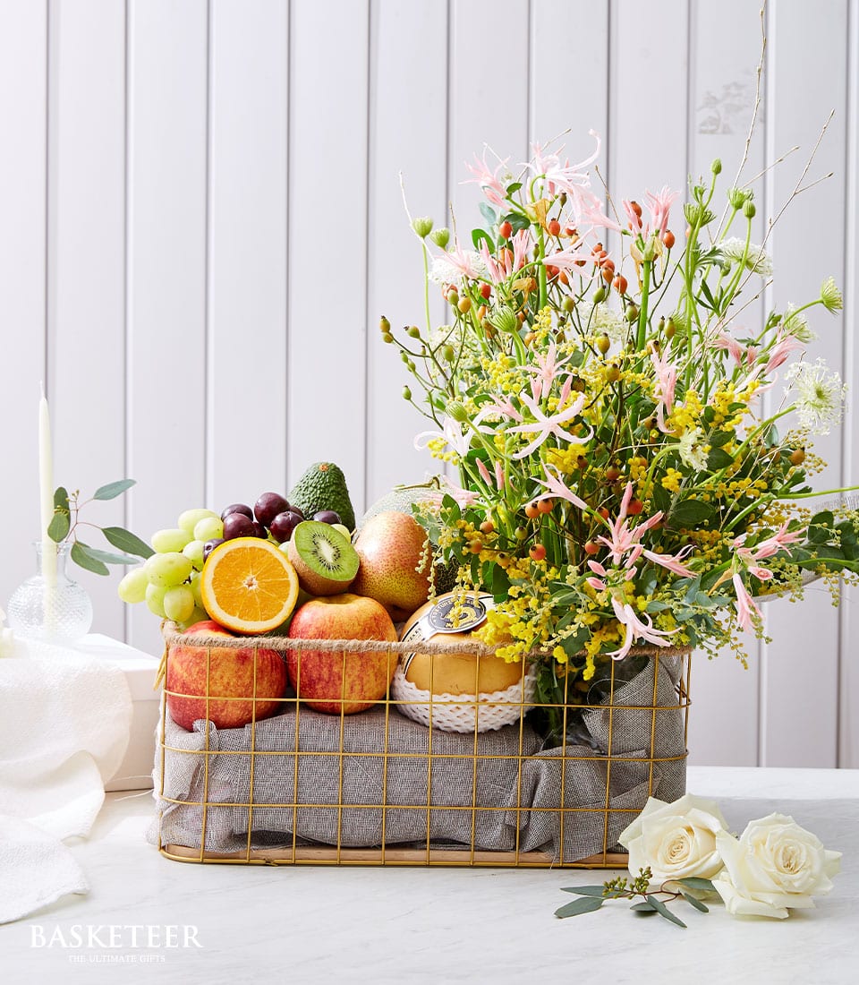Luxury gold wire fruit and flower basket with fresh tropical fruits, pink spider lilies, yellow mimosa, and white roses