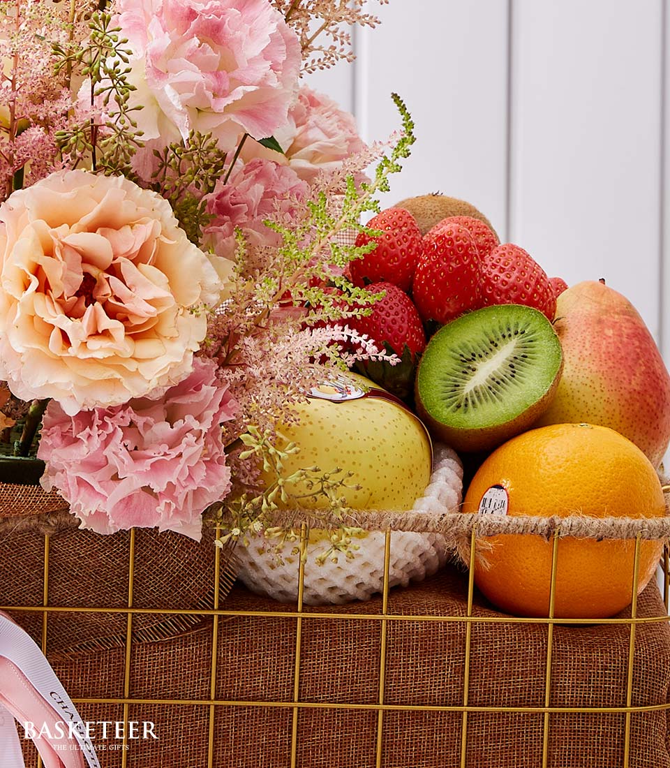 Luxury fruit and flower gift basket with fresh strawberries, kiwi, pear, apple, and orange alongside pink peach blooms in