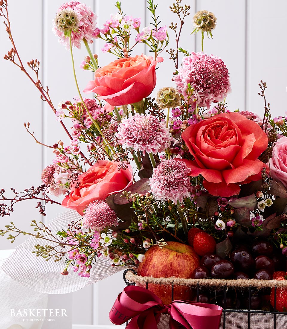 Luxe fruit and floral gift basket with coral roses, pink waxflowers, fresh cherries and strawberries in dark wire basket