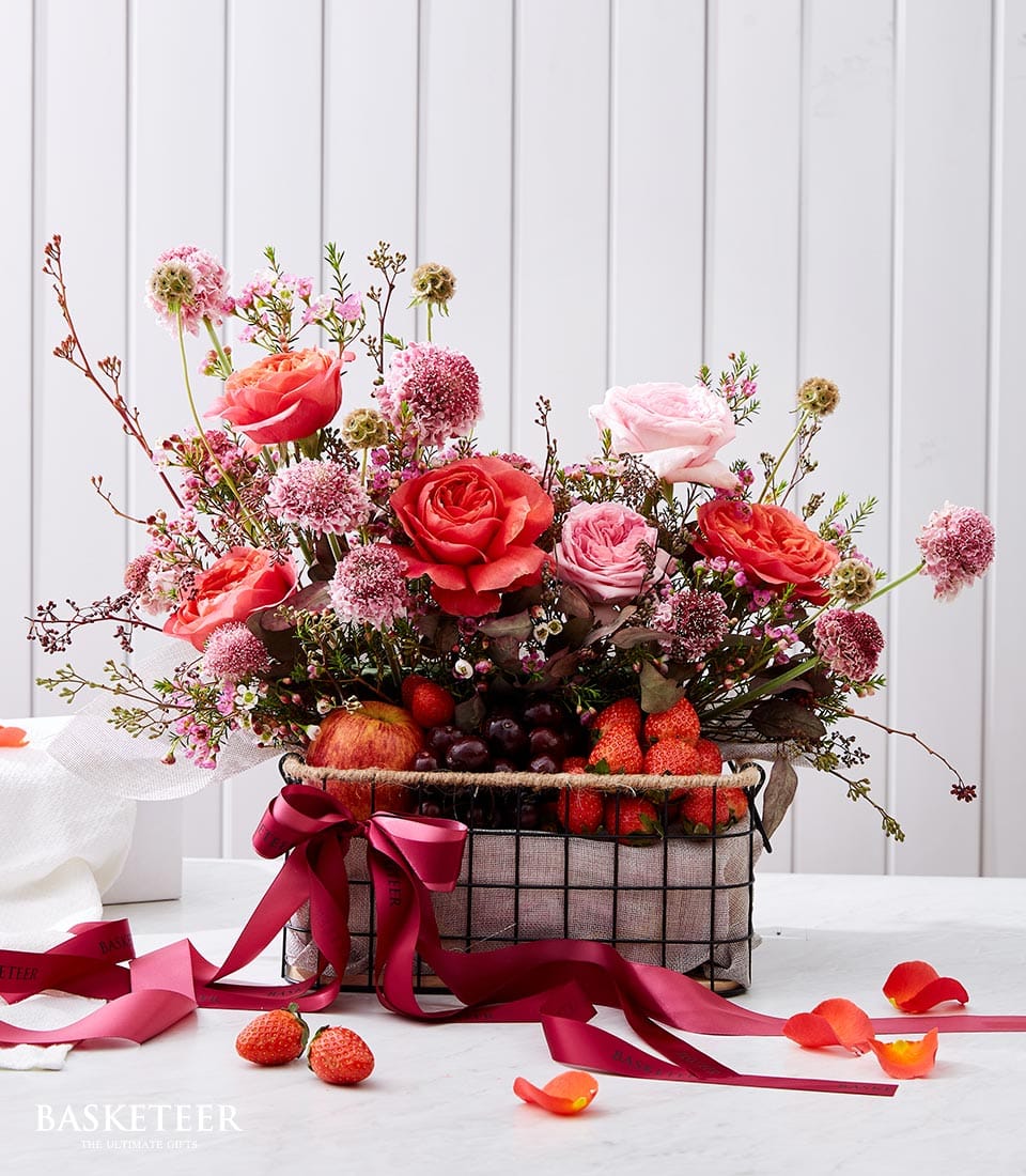 Luxury fruit and floral gift basket with pink and red roses, fresh strawberries, grapes, and apple, tied with red satin