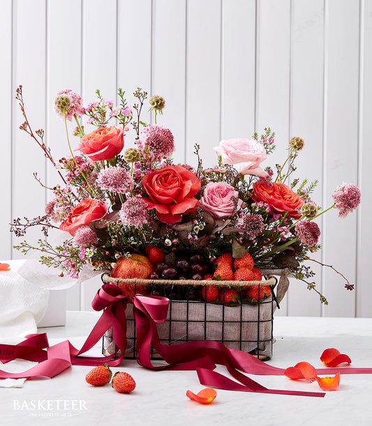 Luxury fruit and floral gift basket with pink and red roses, fresh strawberries, grapes, and apple, tied with red satin