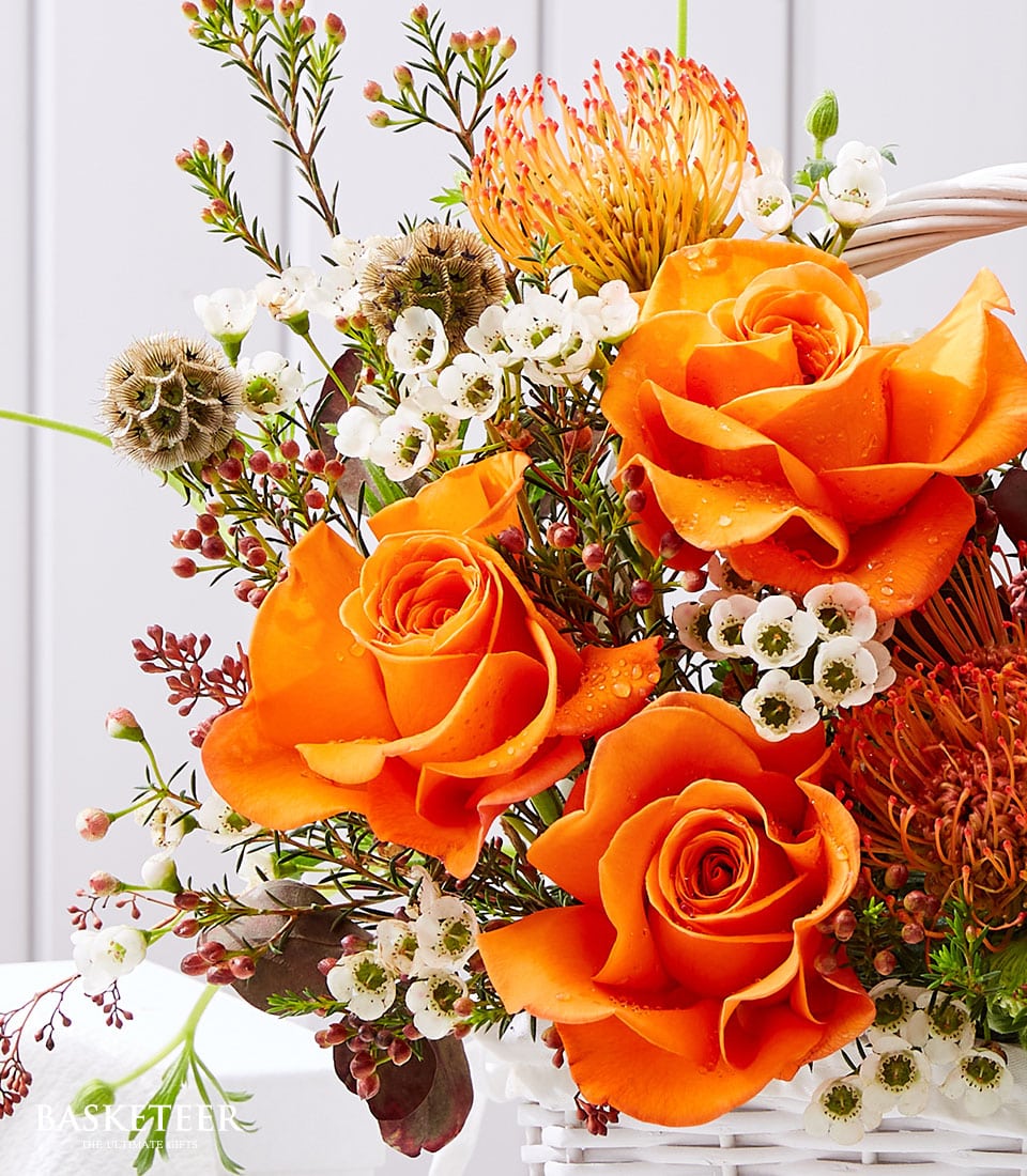 Fresh orange roses with tropical fruit flowers in white woven basket, congratulations gift arrangement