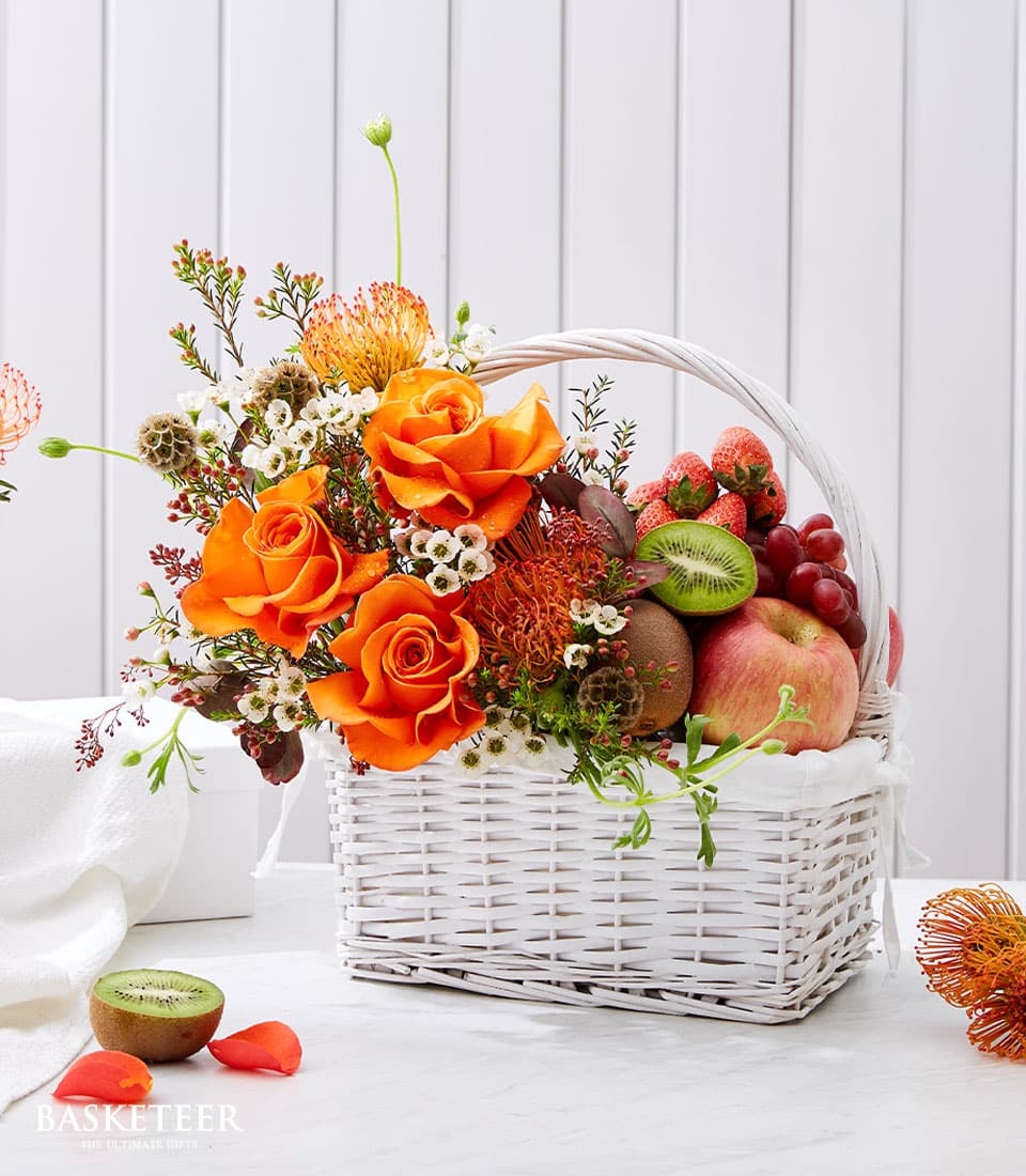 Vibrant orange roses with fresh strawberries, grapes, and kiwi in white woven basket