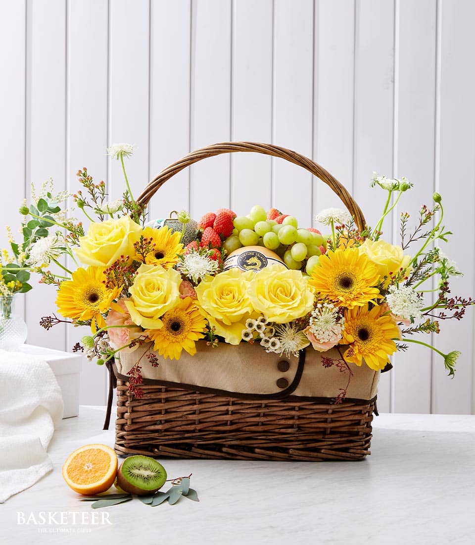 Dark wicker basket with yellow roses, gerberas, fresh grapes and strawberries for luxury fruit and flower gifting