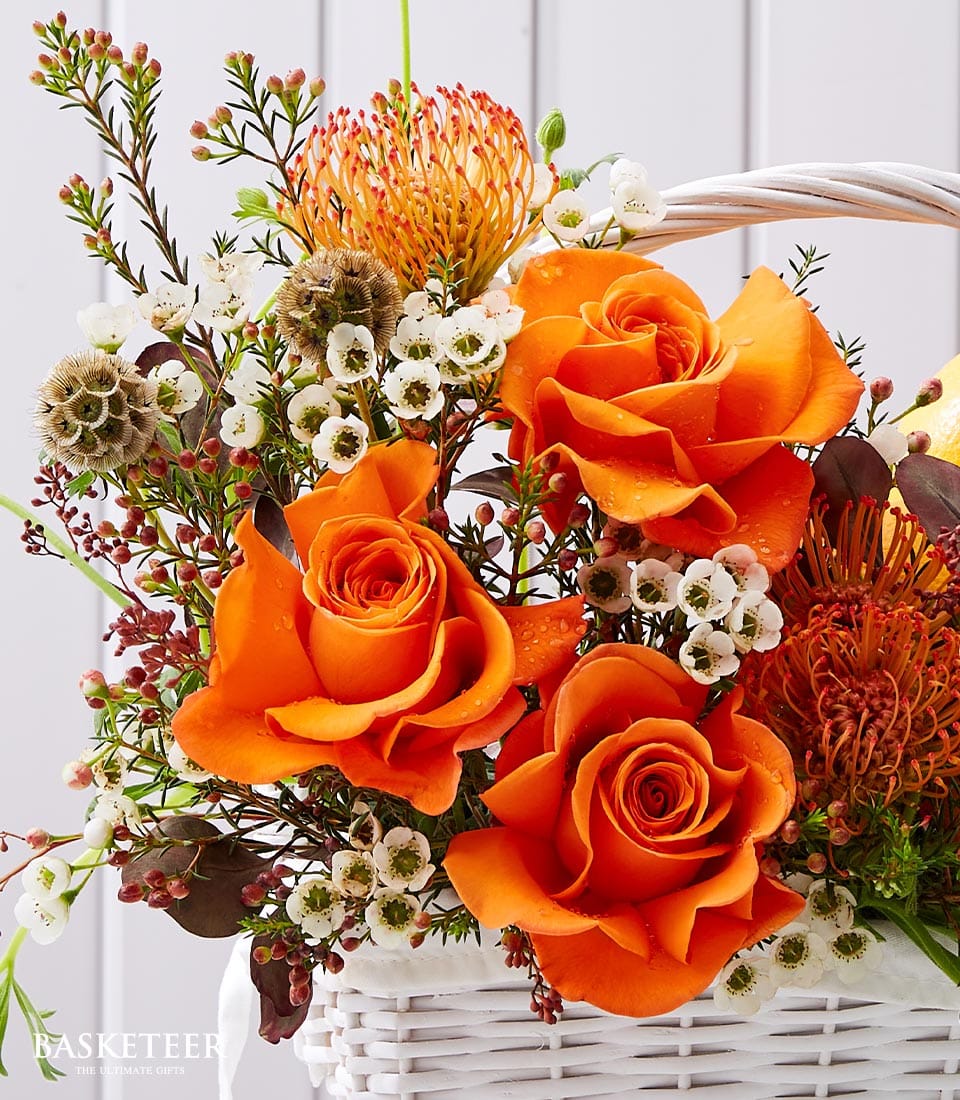Vibrant orange roses and protea flowers in white woven basket with fresh greenery
