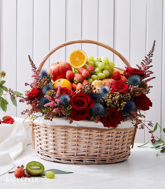 Premium Christmas gift basket with red roses, fresh tropical fruits, and blue thistles in woven wicker