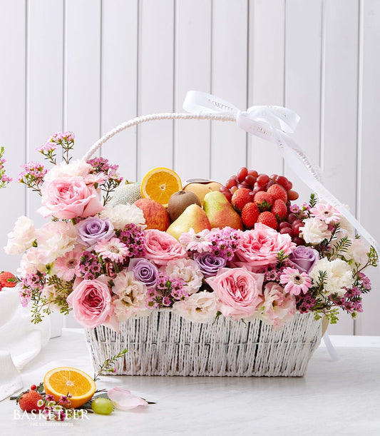 Luxury fruit and flower gift basket with fresh strawberries, grapes, citrus, and pink roses in woven white basket