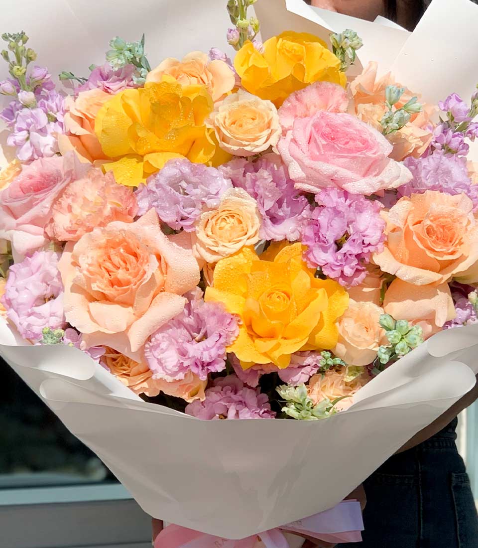 Soft Seasons Harmony bouquet with yellow roses, peach and pink blossoms, lavender accents in white paper wrap for graduation