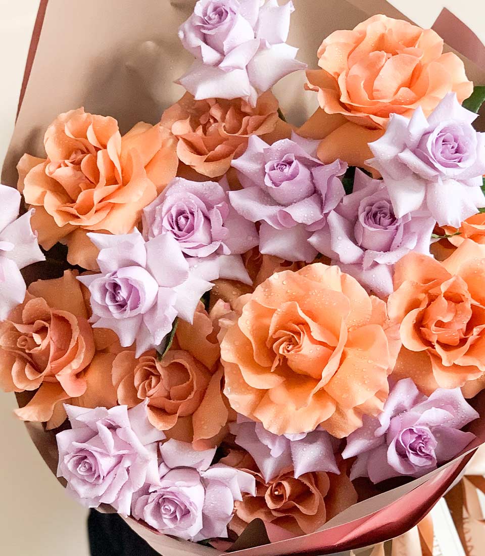 Soft lavender and peachy-orange rose bouquet with water droplets, kraft paper wrap and maroon ribbon