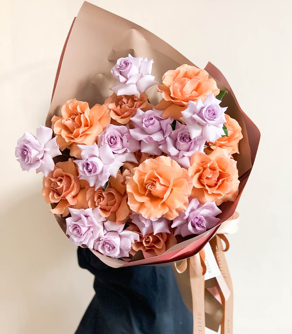 Soft peach and lavender rose bouquet with water droplets, wrapped in kraft paper and burgundy tissue with satin ribbon