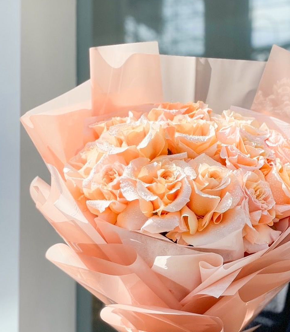 Peach rose bouquet with dewy petals, wrapped in layered blush paper