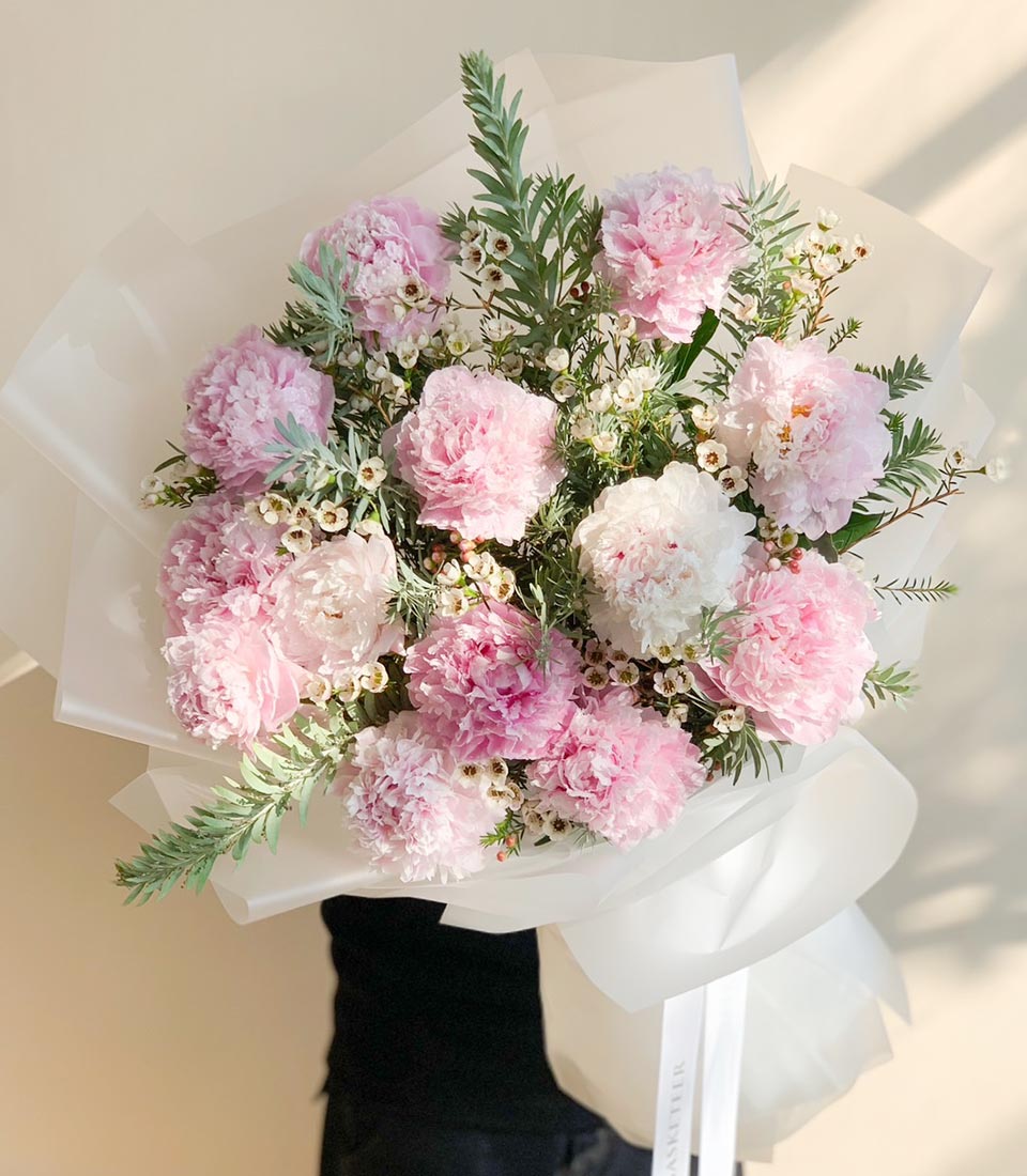 Blush pink and white peony bouquet with green foliage, wrapped in white paper with satin ribbon