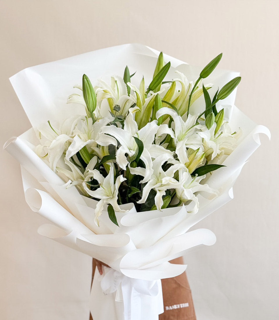 Pure white lily bouquet with delicate open blooms and buds, wrapped in crisp white paper