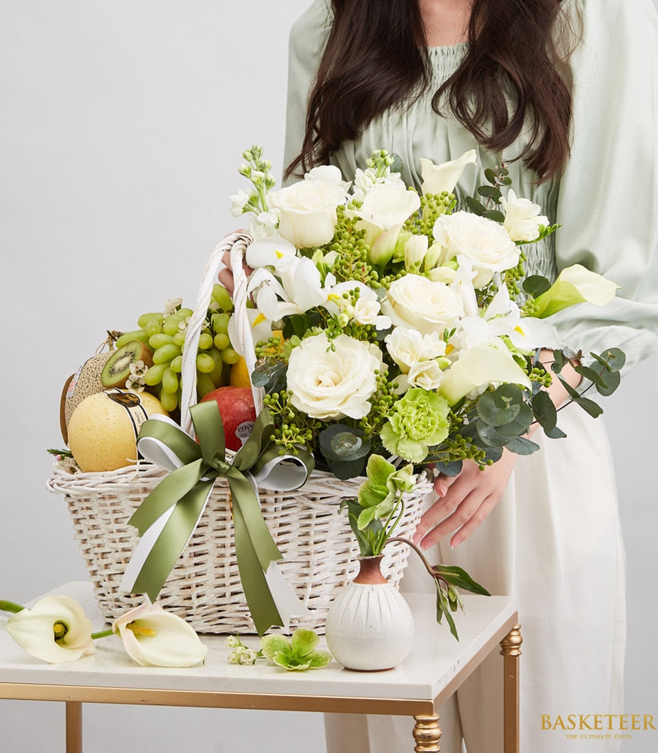 Fresh fruit and white floral gift basket with roses, calla lilies, and seasonal produce in white wicker