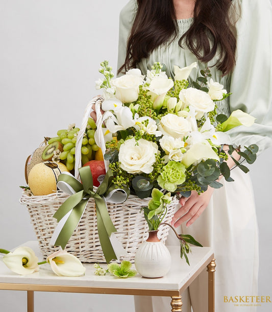 Fresh fruit and white floral gift basket with roses, calla lilies, and seasonal produce in white wicker