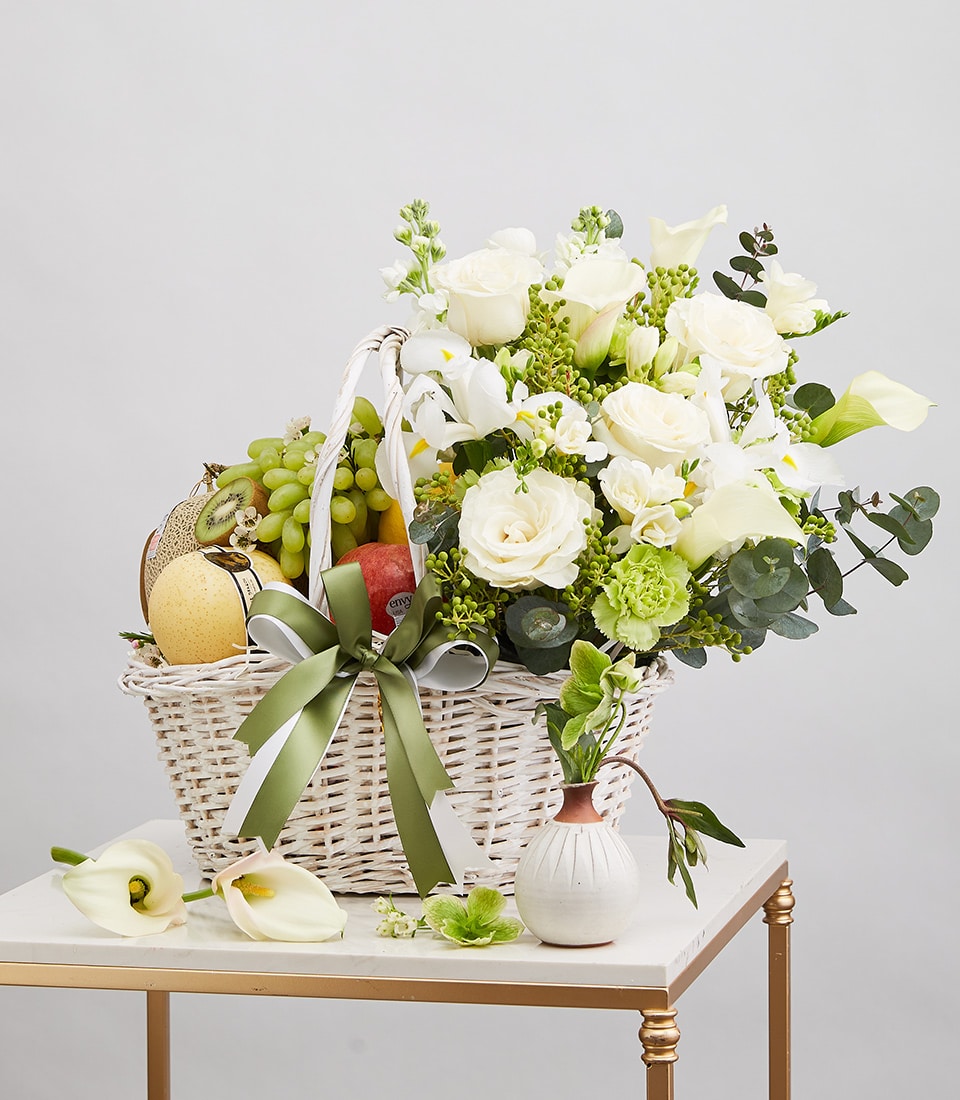 White wicker basket with fresh assorted fruits and white floral arrangement of roses, calla lilies, and eucalyptus