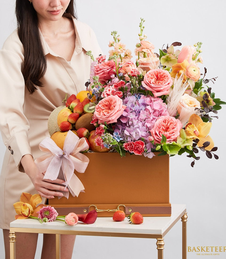 Luxury brown leather gift box with fresh strawberries, kiwi, melon and vibrant pink, purple rose and hydrangea arrangement
