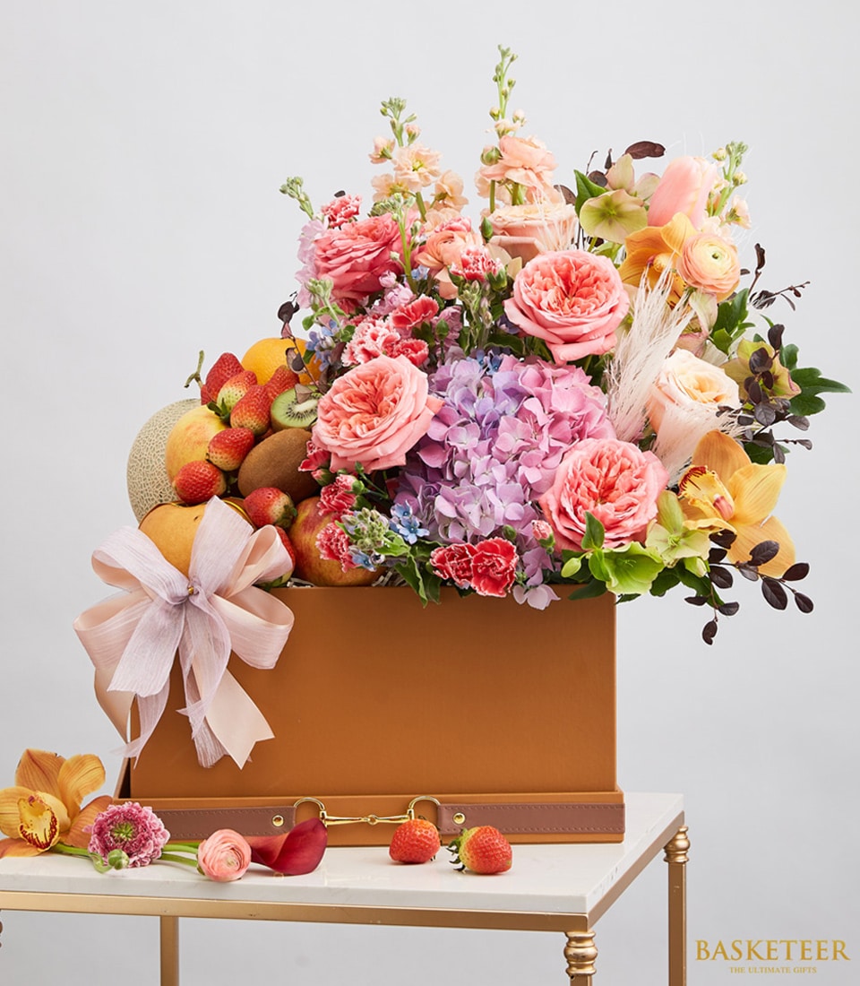 Luxury fruit and flower gift box with pink roses, hydrangeas, fresh strawberries, and tropical fruits in leather