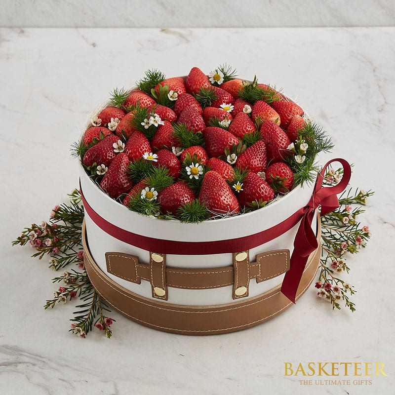 Premium fresh strawberry gift box with white ribbon and leather-look base, topped with white daisies and green foliage