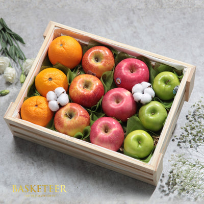 Premium wooden crate filled with fresh oranges, red and green apples, surrounded by cotton bolls and greenery