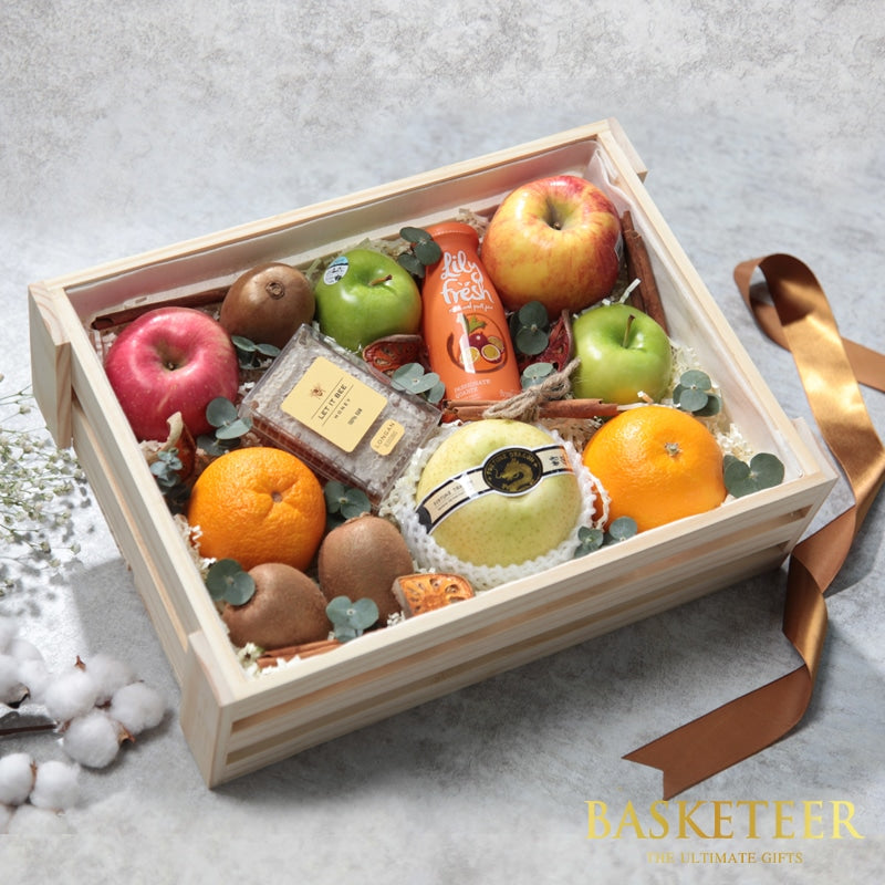 Wooden gift box with fresh apples, oranges, kiwis, pear, Lily Fresh juice, and Let It Bee honey on white shredded paper
