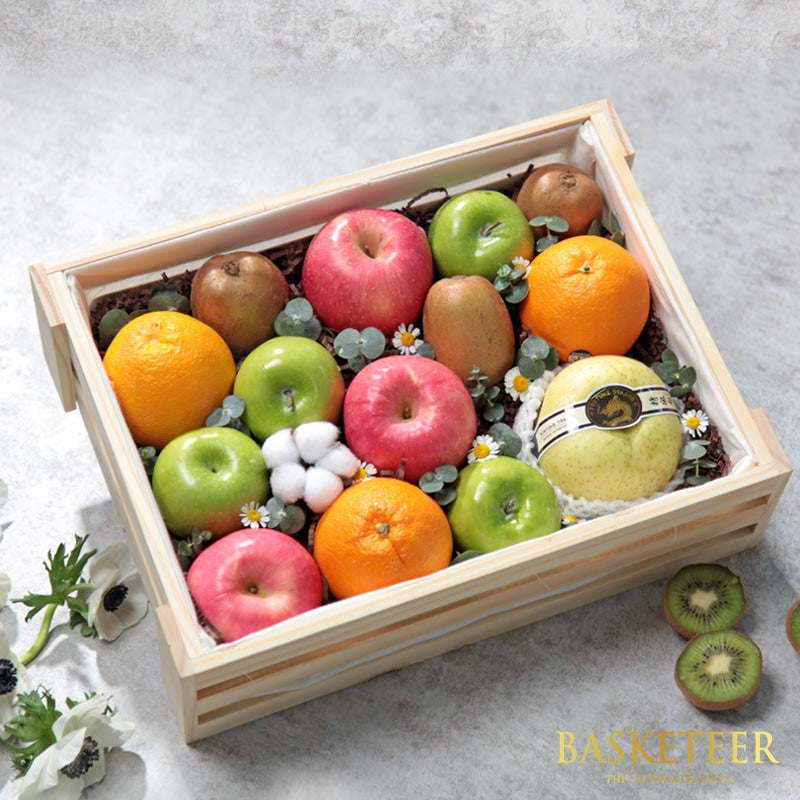 Wooden crate filled with fresh red apples, green apples, oranges, kiwis, and pear nestled in dark shredded paper with white