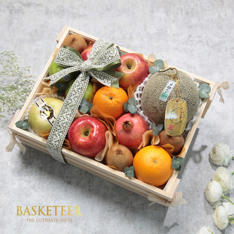 Wooden crate fruit gift basket with apples, kiwis, oranges, pomegranate, pear and cantaloupe tied with green satin and white