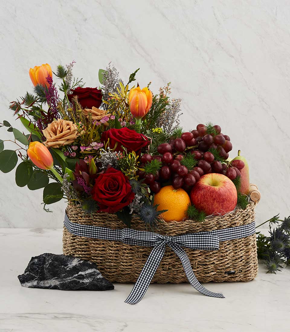 Woven fruit and flower basket with red roses, tulips, fresh grapes, and seasonal fruit for birthday celebrations