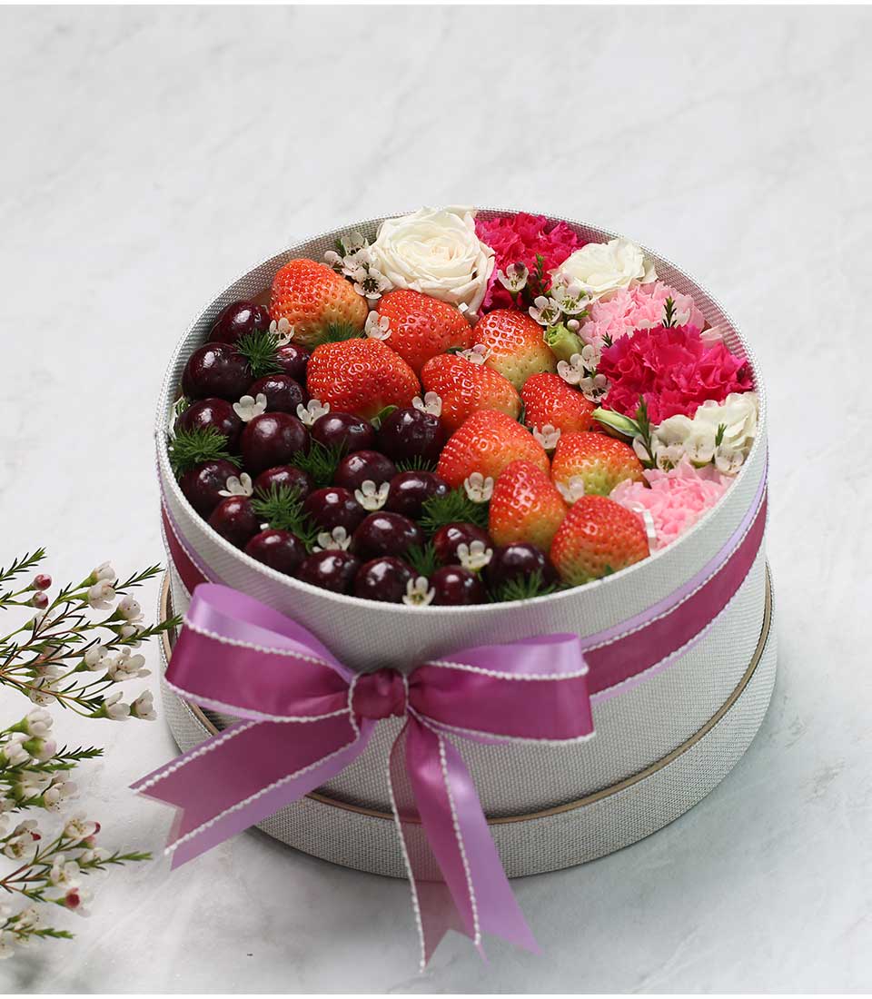 Elegant grey gift box with magenta ribbon filled with fresh strawberries, cherries, roses, and pink carnations