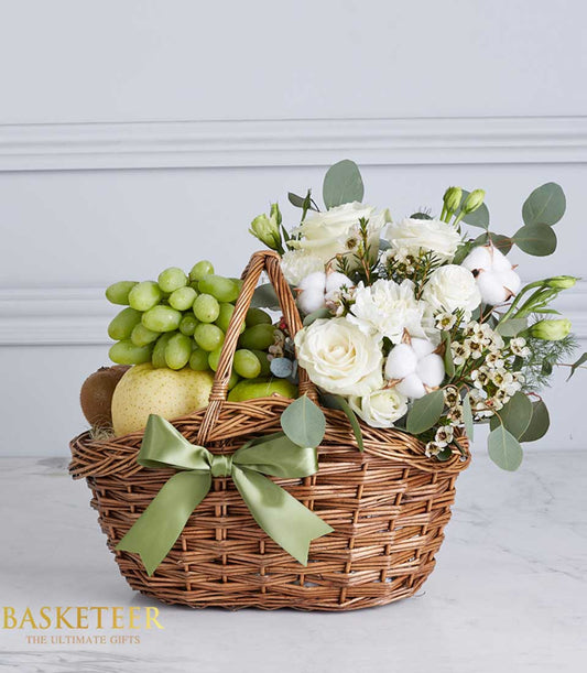 Rustic wicker basket with fresh green grapes, pear, kiwi, apples and white roses with eucalyptus, tied with light green