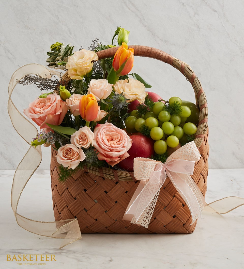 Woven fruit and flower birthday basket with peach roses, orange tulips, grapes, and apples with pink ribbon