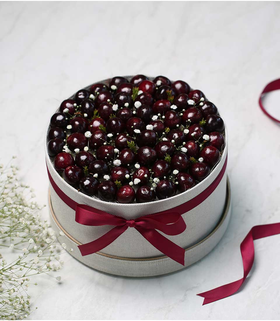 Luxury cherry gift box with dark red fruits, green foliage, and baby's breath, tied with deep red satin ribbon