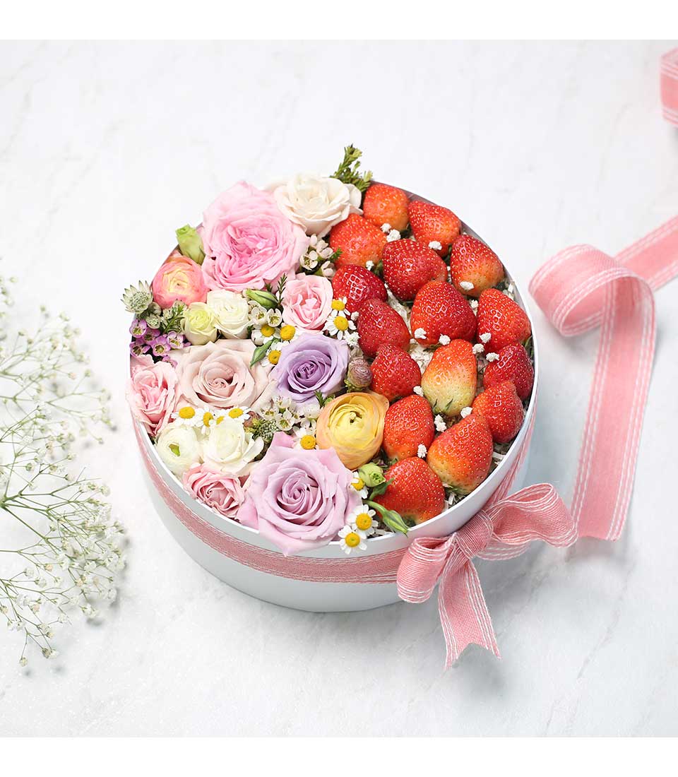 Pastel roses and fresh strawberries in white round gift box with pink striped ribbon