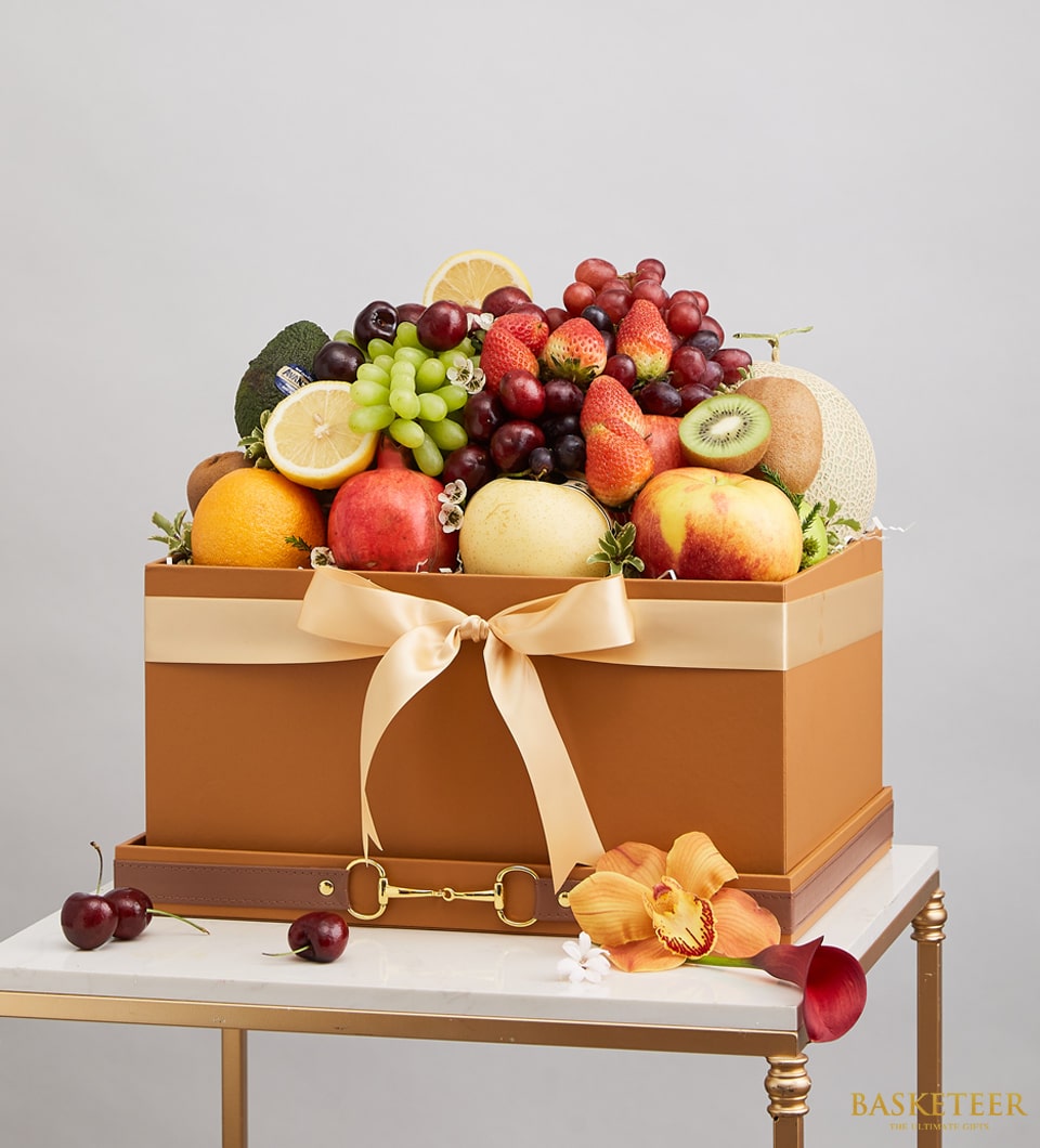 Premium fruit gift box with grapes, strawberries, cherries, and tropical fruits in luxury brown packaging with gold ribbon