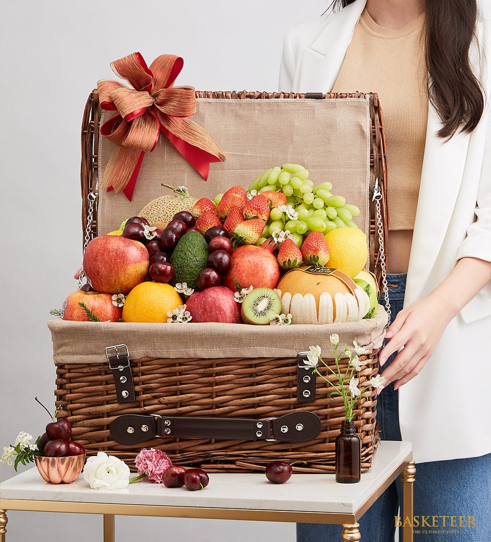 Elegant wicker fruit gift basket with fresh apples, grapes, strawberries, and pomegranates, tied with rustic red ribbon bow